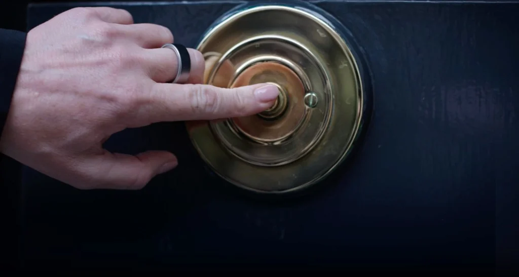 A hand pressing the brass bell at the clinic door